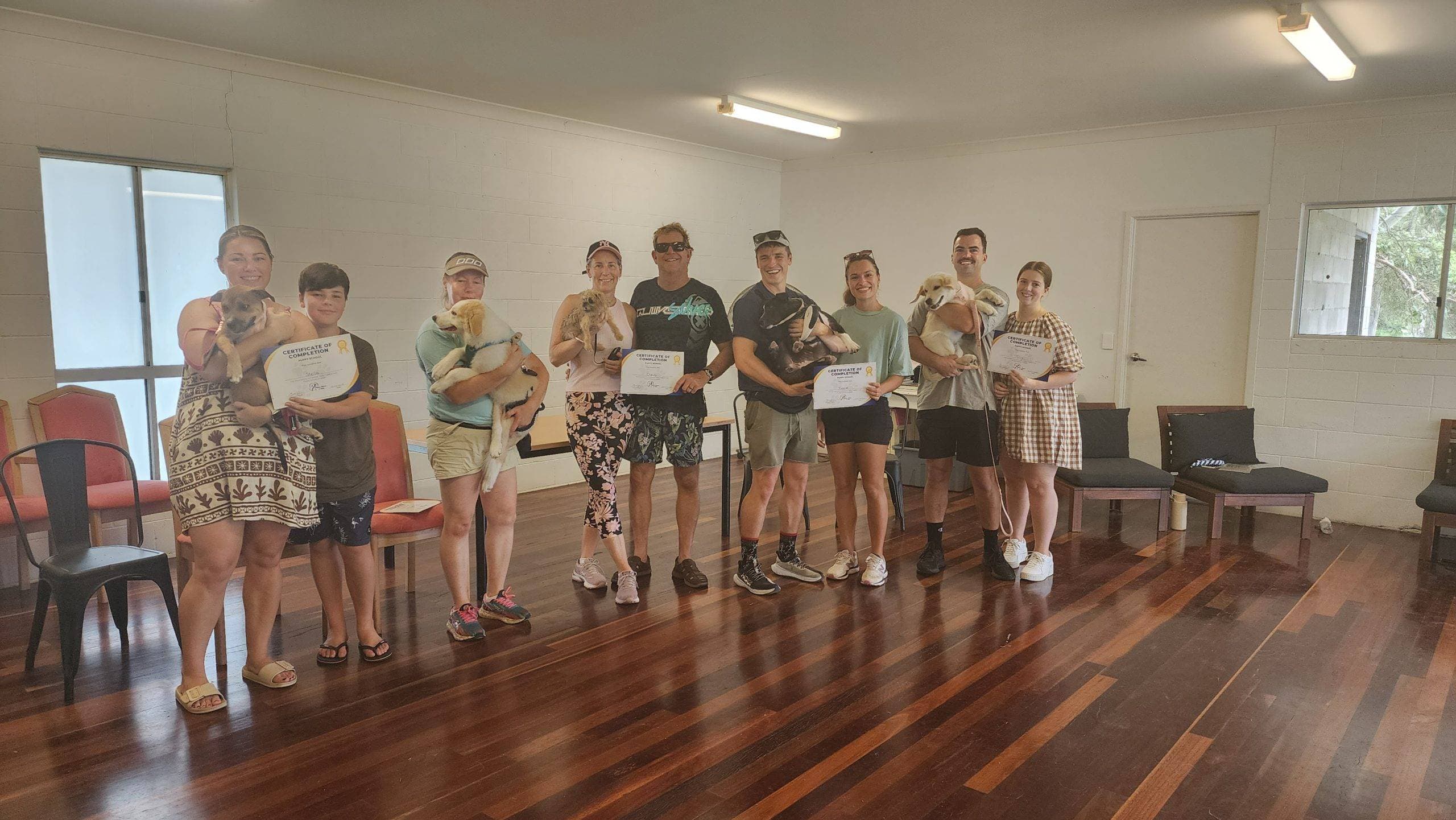 Nine people smiling and holding puppies and certificates at a puppy training school graduation.